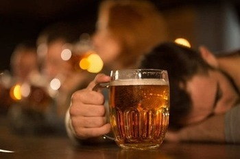Пьяный мужчина с кружкой пива в руке спит на столе